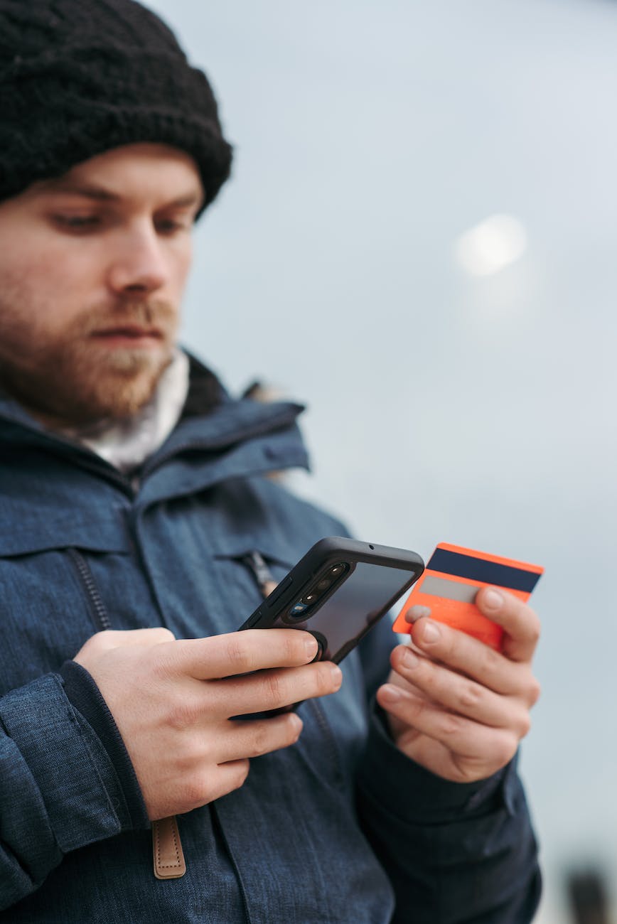 focused male in outwear typing credentials of credit card on smartphone